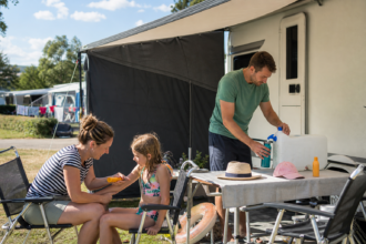 Familie nutzt Markise, Sonnenhüte, Trinkwasser und Sonnencreme auf einem Campingplatz [Bildinhalt mit KI erstellt]