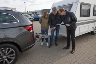 Kaufinteressenten prüfen Zuglast, Anhängerkupplung und Beladung eines Diesel-Zugfahrzeugs [Bildinhalt mit KI erstellt]