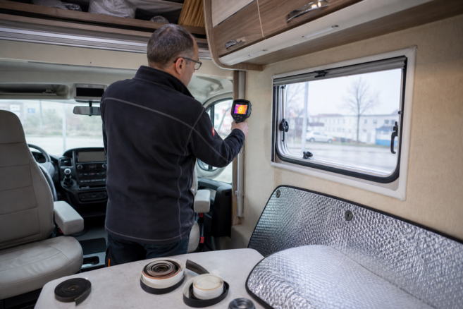Techniker untersucht Fenster und Türdichtungen eines Wohnmobils mit einer Wärmebildkamera [Bildinhalt mit Ki bearbeitet]