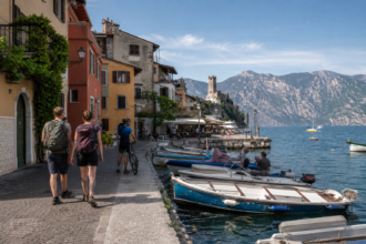 Reisende am alten Hafen von Malcesine mit Blick über den Gardasee [Bildinhalt mit Ki bearbeitet]
