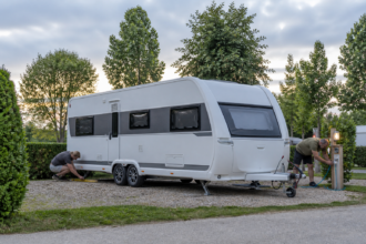 Camper richten einen großen Tandemachs-Wohnwagen auf einem Komfortstellplatz ein [Bildinhalt mit Ki bearbeitet]
