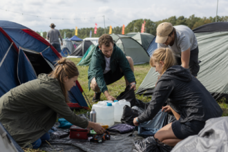 Freunde bauen ihre Zelte auf und sortieren Wasser, Regenkleidung und weitere Festival-Ausrüstung [Bildinhalt mit KI erstellt]