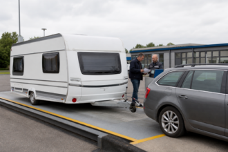 Wohnwagengespann steht vollständig auf einer Fahrzeugwaage während Besitzer und Prüfer die Messung auswerten [Bildinhalt mit KI erstellt]