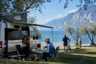 Camper frühstücken auf einem Campingplatz zwischen Olivenbäumen direkt am Gardasee [Bildinhalt mit KI erstellt]