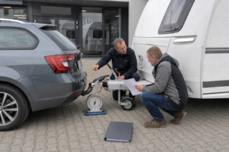 Wohnwagenbesitzer und Fachberater prüfen an Kupplung, Stützlastwaage und Fahrzeugdaten die zulässige Anhängelast [Bildinhalt mit KI erstellt]